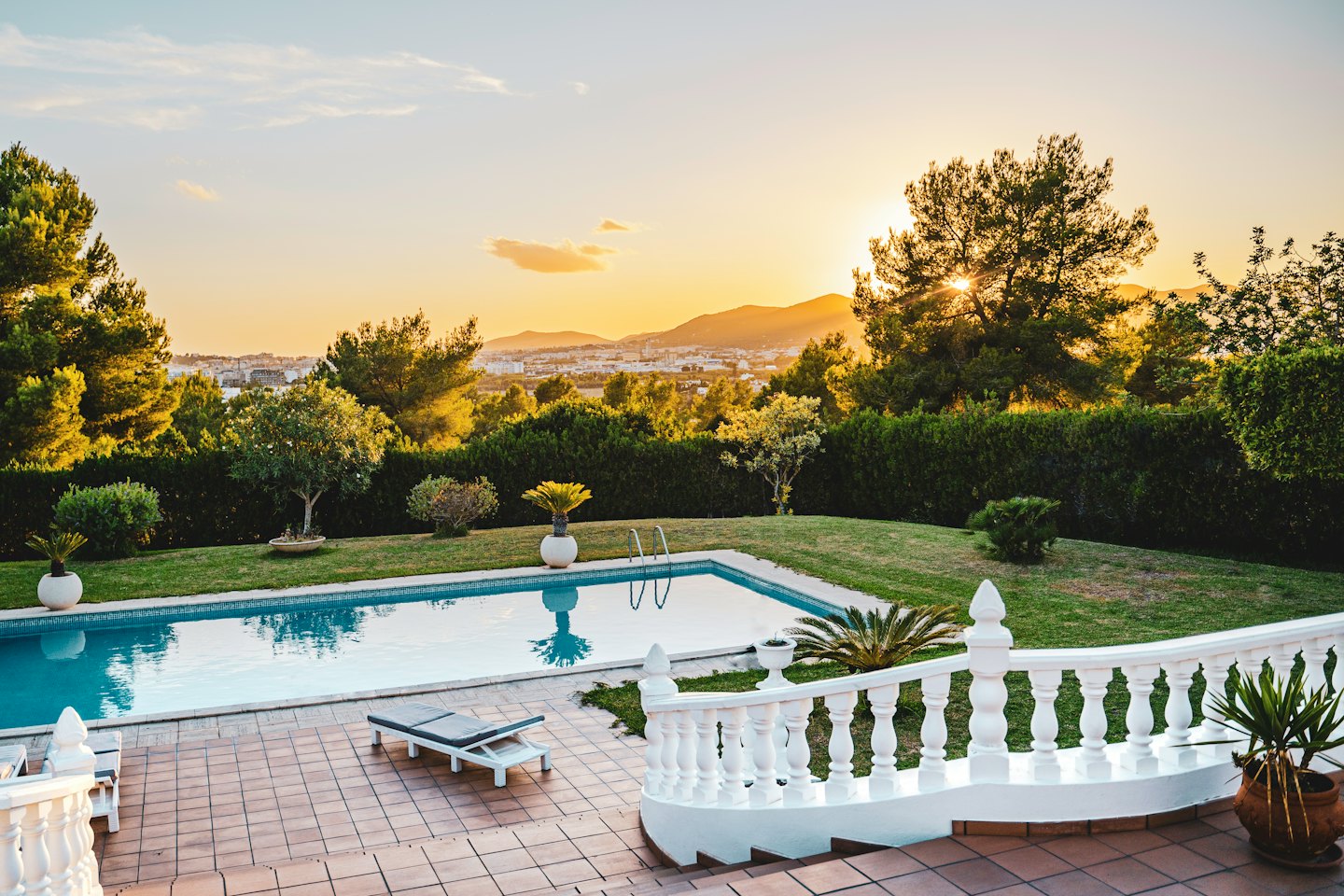 Piscina al tramonto con prato verde e skyline della città.