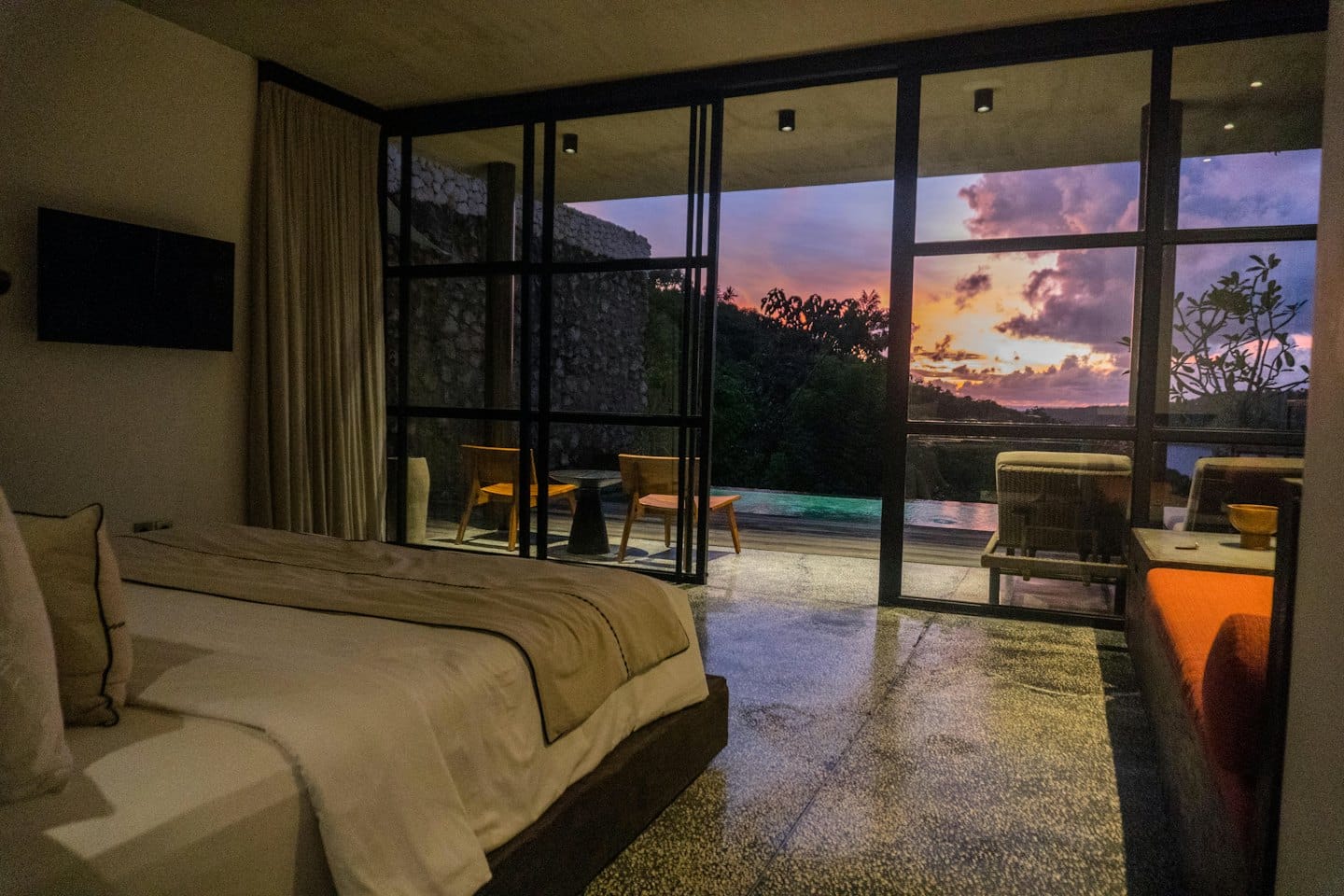 Camera d'albergo di lusso con piscina a sfioro affacciata sulla vegetazione al tramonto.