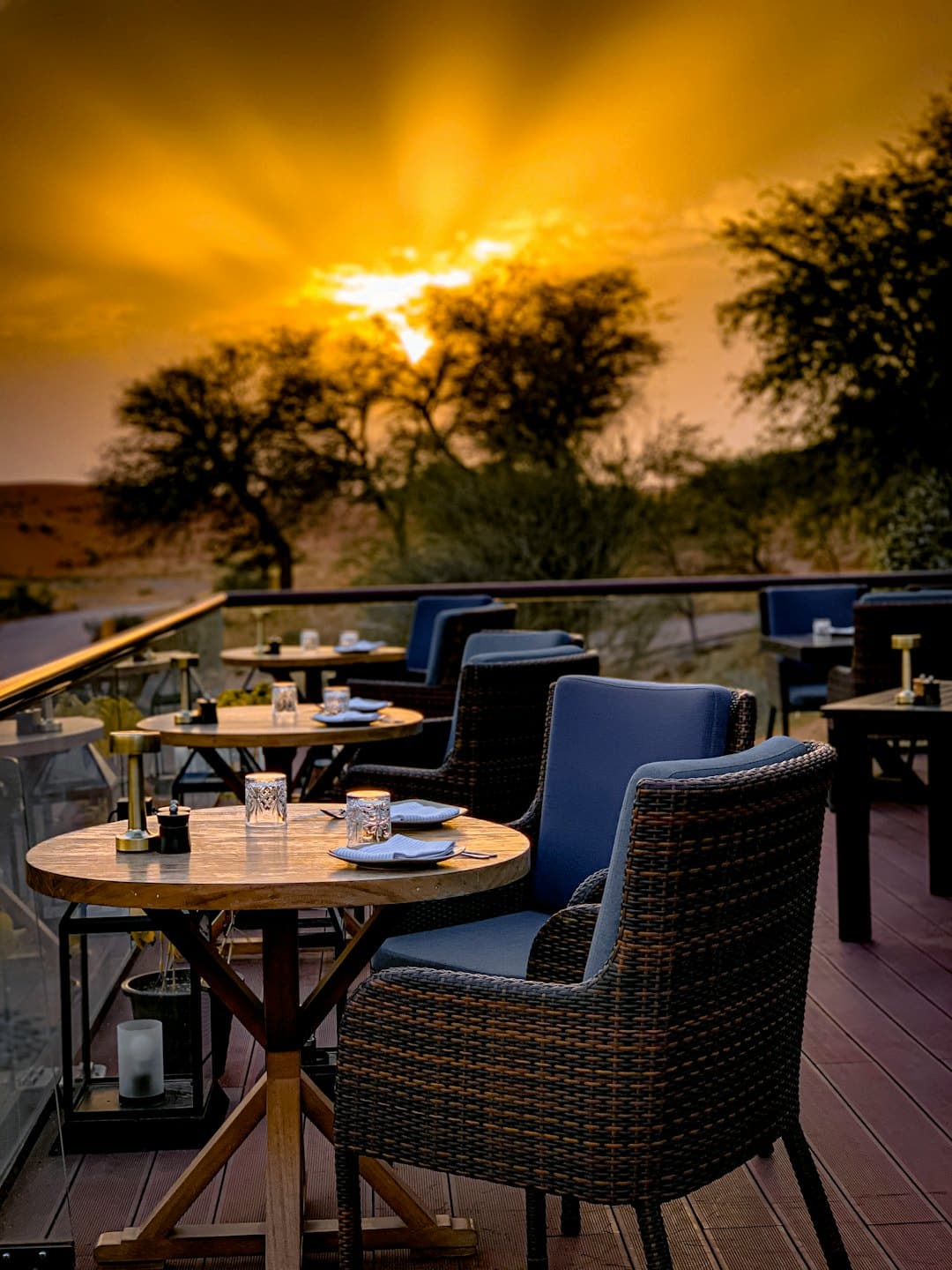 Terrazza di un ristorante all'aperto con tavoli apparecchiati che si affacciano su un paesaggio al tramonto.