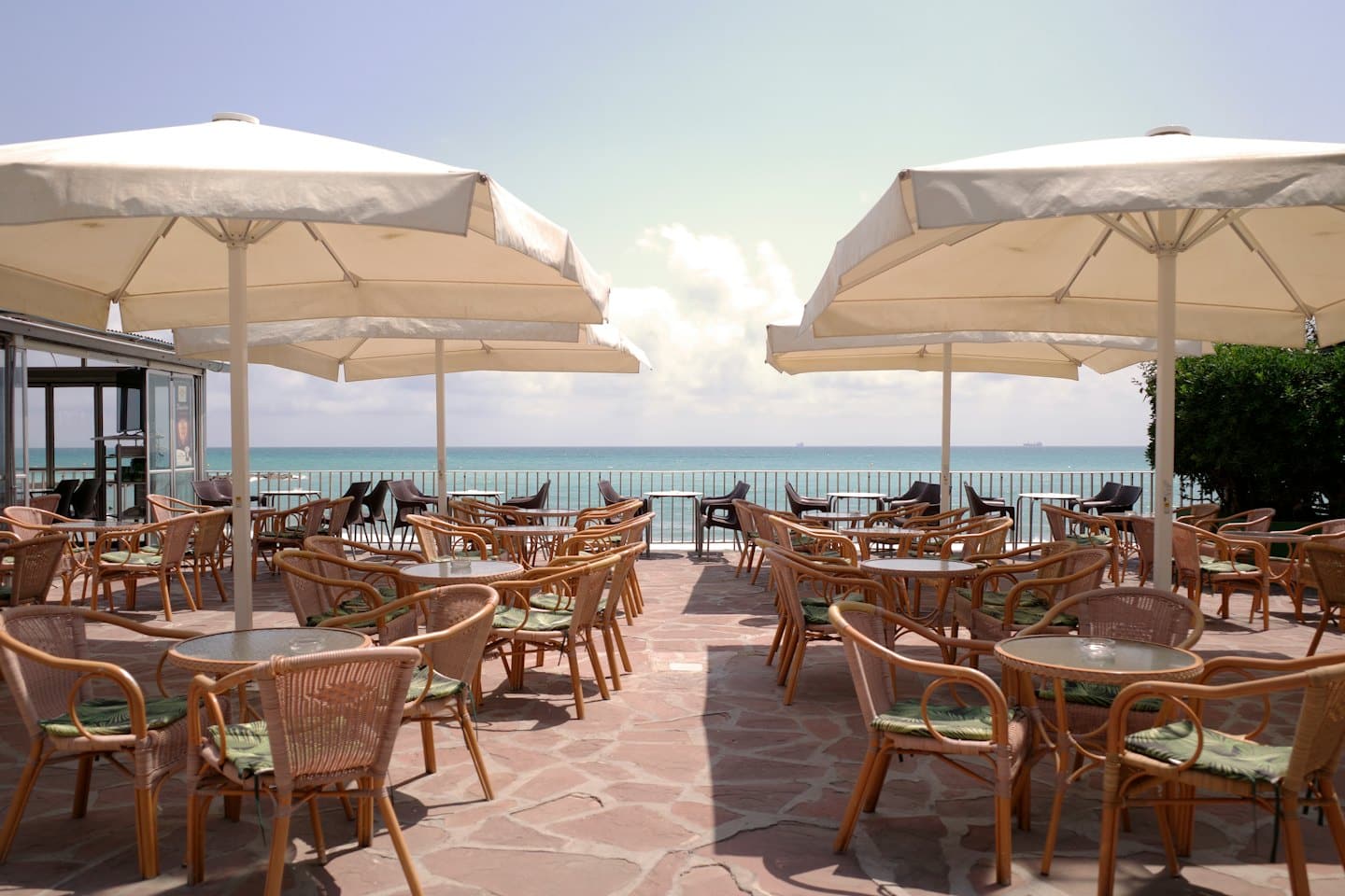 Terrazza vuota di un ristorante sul mare con tavoli, sedie e ombrelloni affacciati sull'oceano.